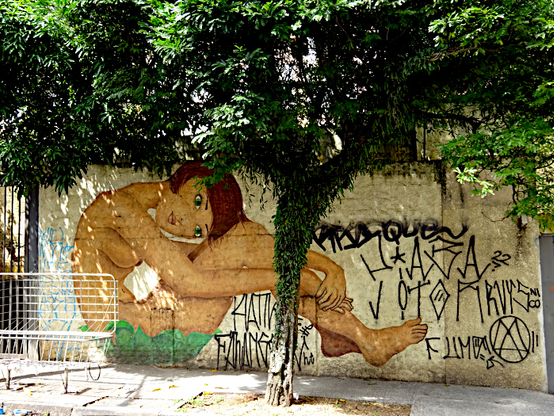 Foto van muurschildering van gebogen zittende vrouw, die onder de op straat staande boom lijkt te zitten