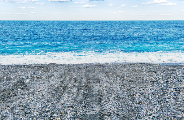Pebble beach with tire tracks leading to the waterline.
