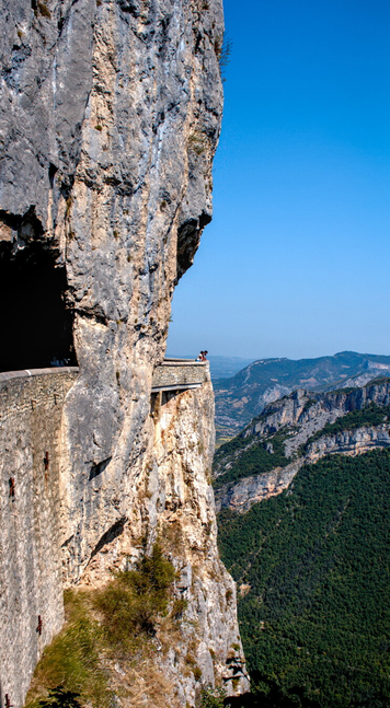 Estrada de montaña, na que dúas persoas están asomadas ó acantilado contemplando el val.  (galego).

Mountain road, where two people are leaning over the cliff, gazing down at the valley.