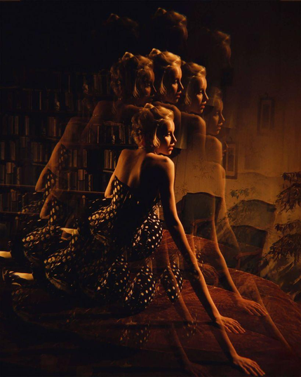 A woman in a polka dot dress poses on a bed, surrounded by softly blurred reflections and a dim, cozy background.