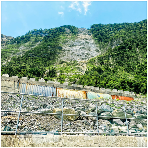 Frog's-eye view of an elevated highway reinforced with rocks and sheet irons in front of a partly wooded hill.