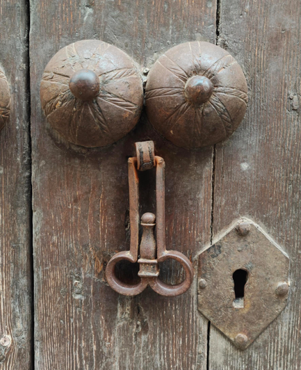 Door knocker, made of two dome-shaped bosses with radial patterns and nipple-like centers, resembling breasts, and a hanging phallic form striker