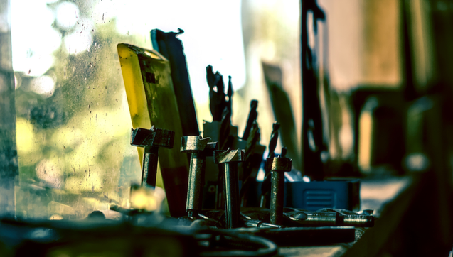 Auf einem Fensterbrett stehen und liegen verschiedene Aufsätze für einen Bohrer, zum Teil in einem Kasten. Das Licht, das durch das Fenster fällt, färbt das Bild in gelbgrüne Töne. 