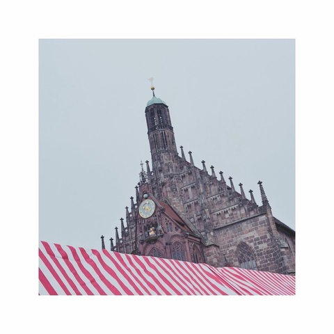 a square images showing the red and white roofs of a christmas market, in the background the dark stone facade of an old church is overlooking the market