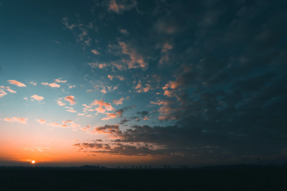 Sonnenuntergang mit dunklem Vordergrund, viel Himmel in pastell und einem winzigen Sonnenball kurz vor weg.