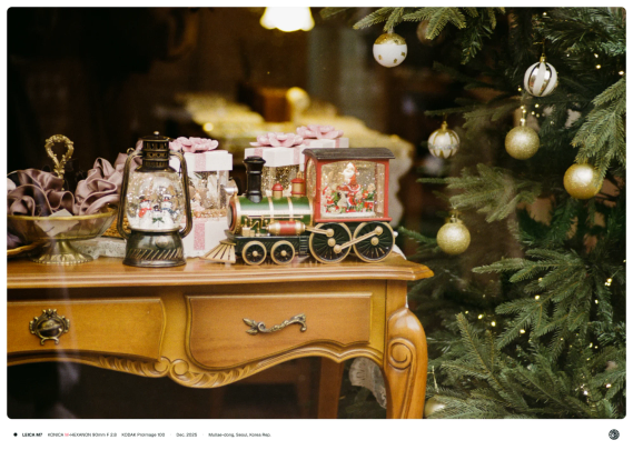 가게의 쇼윈도우로 앤틱한 탁자 위에 올려진 크리스마스 소품과 크리스마스 트리가 보이는 모습.
