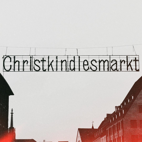 a black and white image of a christmas decoration hanging across the street. the sign us the german name "christkindlesmarkt" to welcome visitors to the christmas market