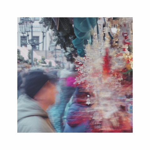 strolling over the christmas market. a square color image is showing some partly blurry christmas decorations in the foreground and and an also blurry visitor watching all the offerings