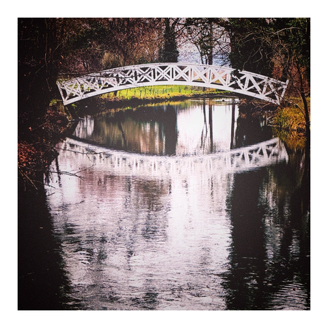 Brücke mit weißem Geländer und Spiegelbild im Wasser, weitere Spiegelungen der Ufervegetation im Wasser