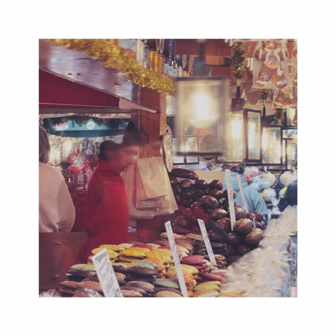 strolling over the christmas market. a square color image is showing some partly blurry christmas decorations, some food and some old school lamps of one of the huts