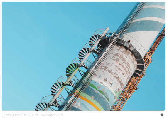 하늘 높게 솟은 콘크리트 기둥에 나선형 철골 계단이 둘러싸고 있는 모습.