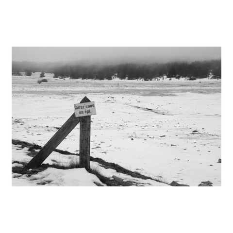 A 'Park at an angle' sign was placed next to a snow-covered, deserted pond. (Version françæ) Panneau 'Garez-vous en épi' plantæ læ long d’æn étang déserx couverx de neige.