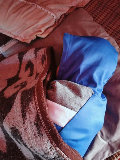 Saji is bundled in a blue hooded sweatshirt and a patterned blanket on a bed.