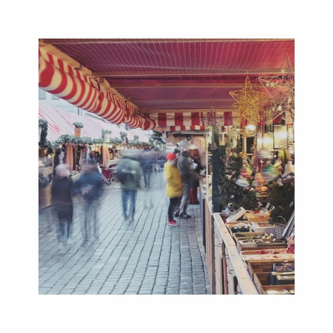 strolling over the christmas market. the square color image is showing a partly blurry alley between the huts. in the foreground a red textile cover with some christmas decorations is building the roof of the frame