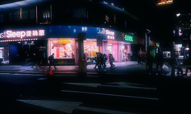 Pedestrians pass outside of a brightly lit 7/11.