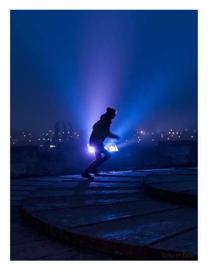 A silhouette of a young person running from left to right, backlit by a powerful blue-purple spotlight.