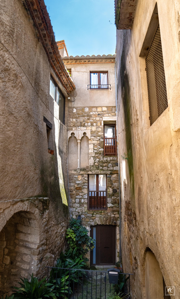 Color photo looking down a short dead end side street in a Catalonian town with buildings on all sides. 