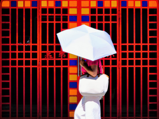 Woman with white remember passing by an red iron gate