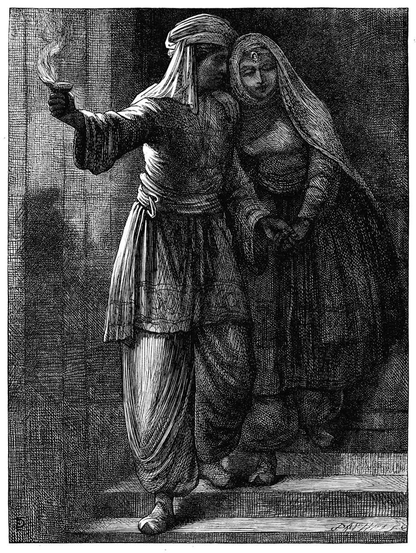 A man wearing a turban holds a woman by the hand and lights the way with an oil lamp as they walk down a flight of stairs.