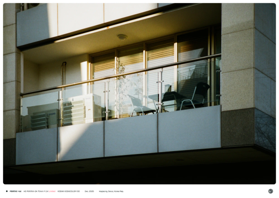 건물에 있는 한 사무실의 테라스. 유리 난간의 좁은 테라스 안에 에어컨 실외기와 간이 의자와 테이블이 있음.