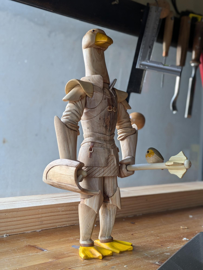 An anthropomorphic goose weraing plate armor. It's holding a shield and a mace. On the mace, red robin sits.
