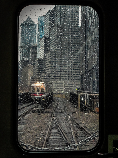 train window with raindrops showing tracks buildings and another train outside the window. blurry outside