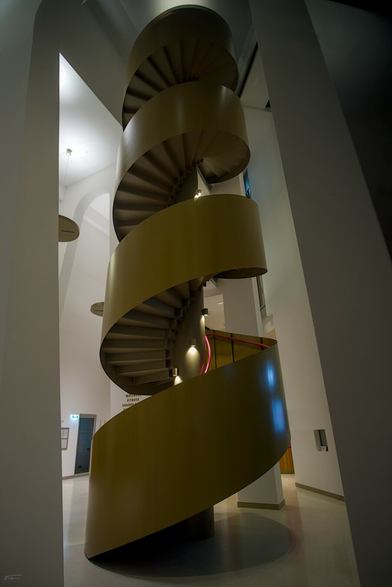 Das Foto zeigt eine moderne, freitragende Wendeltreppe in einem hellen, minimalistischen Innenraum. Die Treppe windet sich spiralförmig nach oben und besteht aus glatten, beige-grauen Elementen, die einen harmonischen und fließenden Eindruck erzeugen. Die Wände und der Boden sind in hellen Farben gehalten, was dem Raum eine offene und luftige Atmosphäre verleiht. Die Beleuchtung ist dezent und betont die klare Linienführung der Treppe. Im Hintergrund sind Türen und ein Teil der Wandgestaltung zu erkennen.
 -------- 
The photo shows a modern, cantilevered spiral staircase in a bright, minimalist interior. The staircase winds upwards in a spiral and consists of smooth, beige-grey elements that create a harmonious and flowing impression. The walls and floor are decorated in light colours, giving the room an open and airy atmosphere. The lighting is subtle and emphasises the clear lines of the staircase. Doors and part of the wall design can be seen in the background.