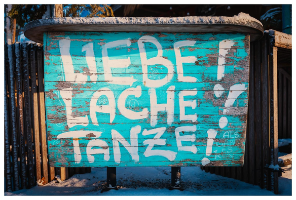 Auf eine azurblau gestrichenen Holzwand steht mit weißer Farbe

LIEBE!
LACHE!
TANZE!