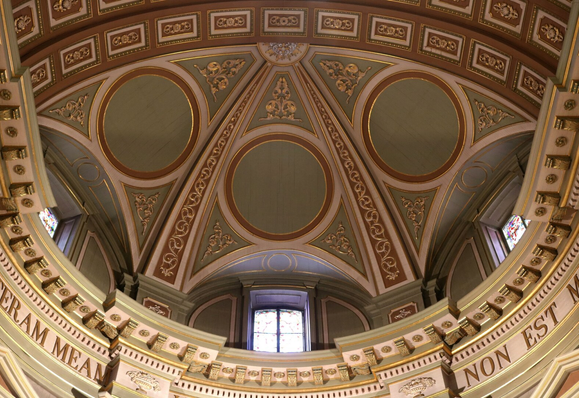 Photograph of one of a cathedral's domes, taken from below and looking upwards, showing half of the dome, with three small windows at its base. The ceiling is adorned with gilded wood carvings set in rectangular, circular, and triangular panels of pale pink and green. The upper sections of the walls supporting the dome, with their carved and circular cornices, are also visible at the bottom of the photograph.

Photographie d'un des dômes du plafond d'une cathédrale, prise du dessous et en regardant vers le haut, montrant la moitié du dôme, avec trois petites fenêtres à la base du dôme. Le plafond est orné de décorations dorées sculptées en bois, placées dans des panneaux roses et vert très pâle rectangulaires, circulaires et en triangles. Le haut des murs soutenant le dône, avec ses corniches sculptées et circulaires sont aussi visibles, dans le bas de la photo.