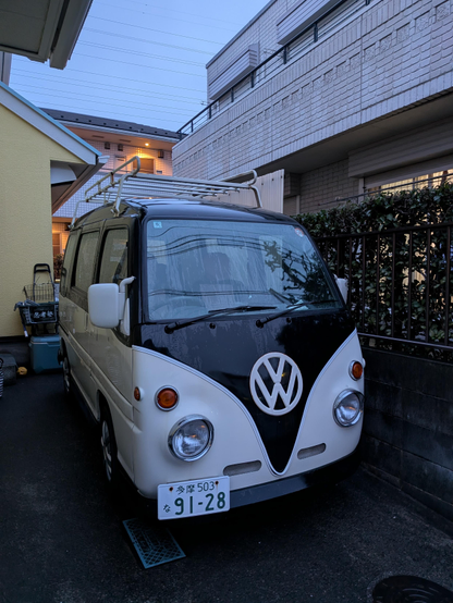 Ein schwarz-weisser VW Bully steht geparkt vor einem Haus in Takao.