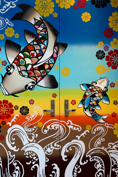 This is a colour street photo in portrait format of a double door decorated in a psychedelic style. 5th Ave NYC (2012).

This double door is hinged on the outside edges with the two handles in the centre. Both doors have a background colour that transitions vertically from black at the base through brown, red, yellow, green, light blue than darker blue at the top. At the base of both doors is a scene of either white Octopus tentacles, plants or breaking waves ? - Think psychedelic. Scattered randomly about both doors are flower heads in various sizes in black, yellow and red. In the upper half of the left door is a large fish, maybe a Carp, with large crescent shaped scales filled with the flags of many nations. In the centre of the right door is a further, smaller fish, it's crescent scales just multi-coloured, no flags. 

During drinking hours this is the street level entrance to a bar downstairs. The art work appears to be changed at regular intervals. 

The location: 5th Avenue, New York City. 