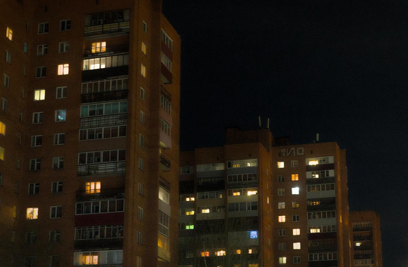 The photo shows a row of identical multi-story buildings late in the evening. Lights are on in some of the building windows.