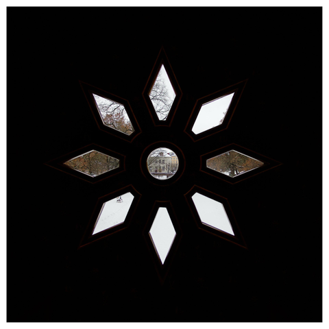 En fyrkantig bild på ett fönster format som en blomma. Genom gluggarna ses hus och träd en bit bort.