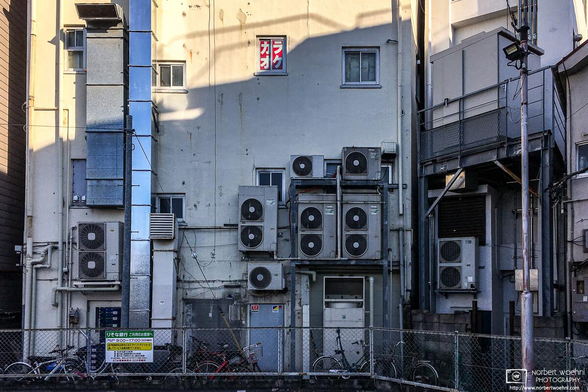 Air conditioning units, chimneys and a red karaoke sign in a window on the back side of a building in the Itabashi Ward of Tokyo, Japan.