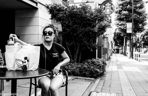 Dona jove amb ulleres de sol asseguda en una terrassa d'un cafè.