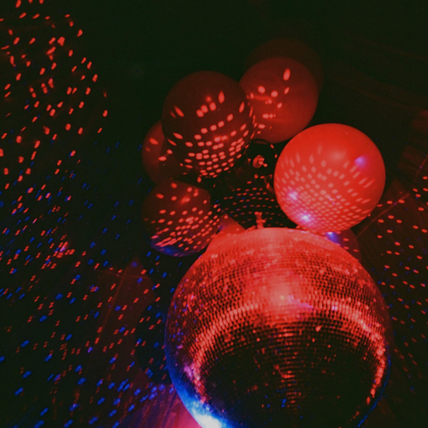 Abstract photograph of a red and blue tinged disco ball and balloons from below.