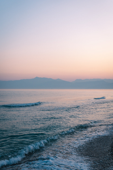 The sea, calm waters on the shore, mountains belonging to Albania visible in the background.