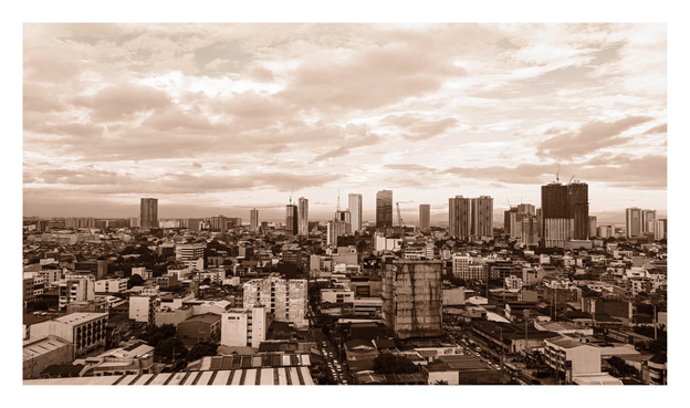 A dense urban cityscape. The image features a crowded foreground of low-rise buildings, residential structures, and streets, transitioning into a background skyline of modern high-rise skyscrapers and construction cranes. A vast, dramatic sky filled with textured clouds dominates the upper half of the frame. - Google Gemini 3 Pro Preview