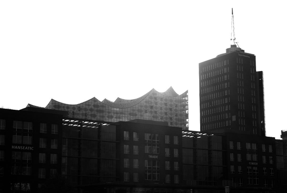 Die Elbphilharmonie im Vordergrund das Columbushaus und das Hanseatic Trade Center. Rechts ein Hochhaus. Das Foto ist schwarzweiß und gegen die Sonne, wodurch der obere Bereich überblendet.