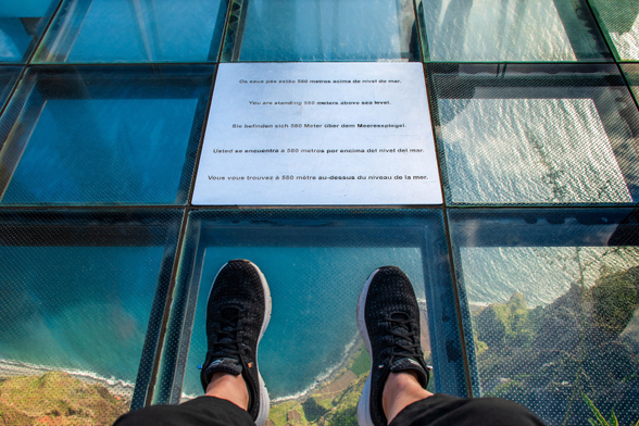 Eine Person steht auf einer Glasplattform hoch über dem Meer.