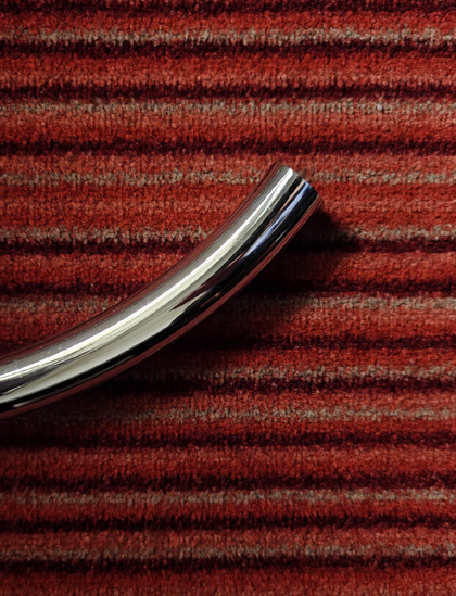 A photo showing a small piece of a curved chrome metal tube on a red striped carpet.