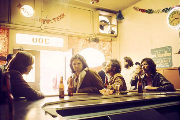 les Doors dans un bar avec des bouteilles de bière, Jim Morrison accoudé au comptoir, portant la célèbre peau de mouton qui a largement contribué à faire de lui un sex-symbol
