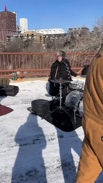Dozens of drummers with their various kits on a snowy bridge