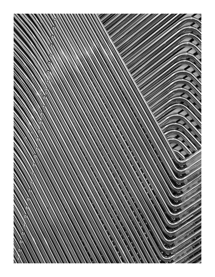 Close-up photograph of tightly packed, parallel metal rods or tubes, with repeating bends and curves visible along the right side, forming a dense, geometric pattern.