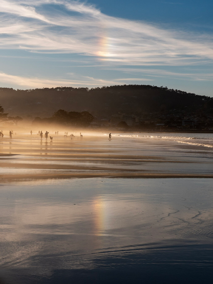 A sun dog in the clouds with its reflection on the wet shore of the beach
