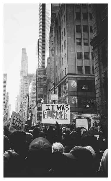Black and white photo. Protesters fill an avenue under the towering skyscrapers of Manhattan. A couple of signs are held up above the crowd, notably one that reads “IT WAS MURDER” and is the focal point of the image. While most people have their backs to the camera, a white-haired person with their lower face concealed faces the viewer and stares intently off to the side.

Taken during the January 11, 2026 NO KINGS protest in NYC in response to the murder of unarmed observer Renee Nicole Good by an ICE agent in Minneapolis. But the sign’s message could apply to any ICE killings before or since, including the January 24 murder of nurse Alex Pretti.