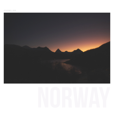 Morning light glows behind distant mountains. A hint of water in the foreground. The frame is mostly black.