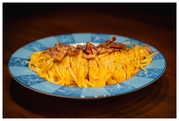 Ein Teller auf dem aufgerollte Spaghetti mit Speckstückchen drauf liegen.