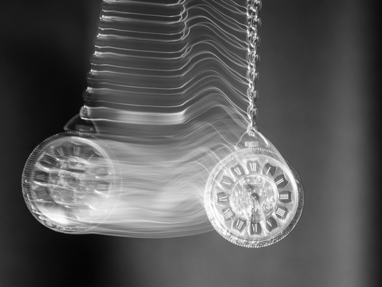 Black‑and‑white photograph of a pocket watch in a pendulum motion.