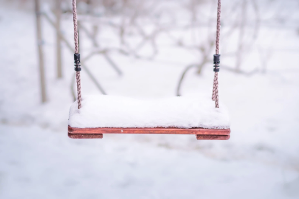 Im Vordergrund der untere Teil einer Schaukel, mit Schnee bedeckt. 
Ringsrum Schnee. Im Hintergrund Schnee mit einigen blattlosen Wrinstöcken.